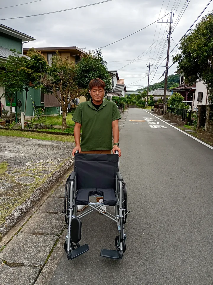 所長・看護師 鍋田尊宏。車いすとともに立つ様子